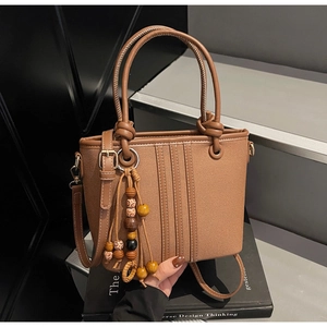 Détail du sac seau en cuir marron avec texture grainée et breloque à pampilles en perles