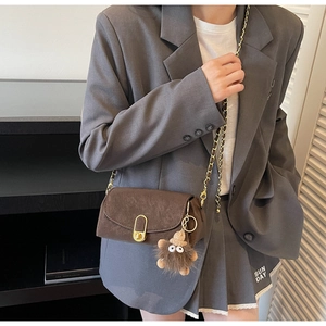 Détail d'un sac bandoulière marron mat avec chaîne dorée et breloque peluche monstre