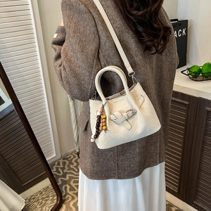 Chic cream quilted tote bag with herringbone pattern and beaded charm shown on shoulder