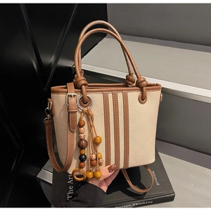 Détail du sac seau en toile avec garniture en cuir marron et pompon en perles de bois