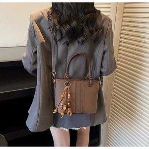 Vue de dos d'une femme portant le sac seau marron foncé avec pompons en perles bois