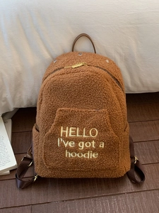 Brown fuzzy fleece backpack with yellow embroidery on white pillow background