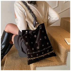 Detail of black suede tote bag with golden floral beadwork and silk scarf wrapped strap