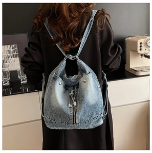 Détail d'un sac à dos en denim bleu clair avec texture souple et délavage vintage sur modèle