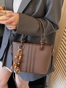 Sac seau en cuir marron avec pompon en perles de bois et double poignée porté par mannequin