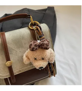 Detail van een pluizige beige teddyhond pluche hanger met luipaardstrik op een bruine tas