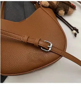 Detail of brown litchi pattern leather bag with adjustable strap and bear pendant