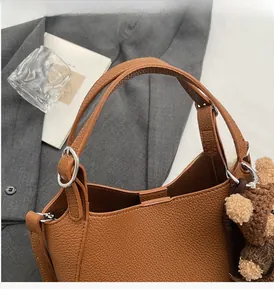Brown lychee leather bucket bag with top handle, side metal ring, and bear charm detail