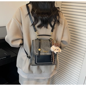 Detail van grijze retro tas met zwarte klep, parels en pluchen hondenhanger op model