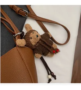 Detailed view of a brown plush bear charm with knitted sweater on a lychee leather bag