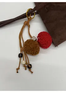 Detail of red and brown plush ball charm with textured beads on a leather handbag