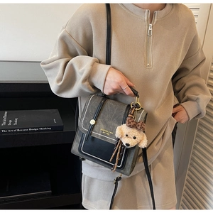 Detail van grijze vintage crossbodytas met pluchen puppy-hanger en merkletters