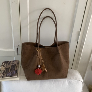 Détail d'un grand cabas en daim marron avec fines bandoulières et pendentif décoratif