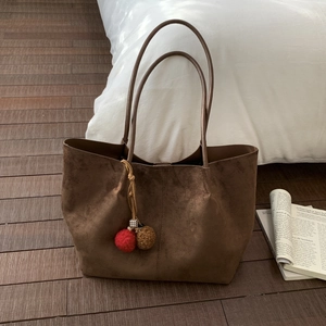 Détail d'un grand sac cabas en daim marron avec pompons sur un sol en bois rustique