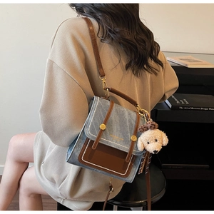 Detail van vintage blauwe canvas crossbodytas met teddybeer-bedeltje en gouden logo