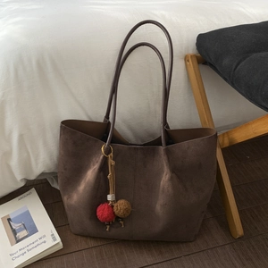 Grand sac cabas marron foncé en daim avec pompon décoratif sur un sol en bois chic