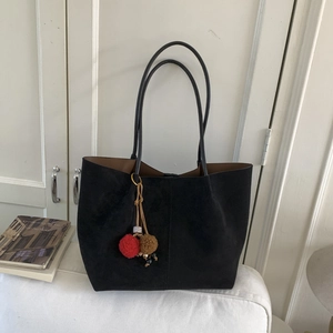 Détail d'un sac cabas en daim noir avec pompons en peluche sur un coussin blanc doux