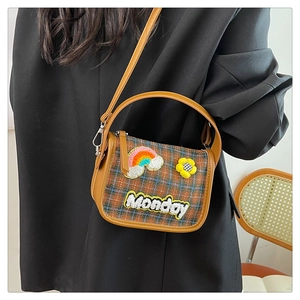 Detail der Retro-Karo-Umhängetasche mit Monday-Regenbogen-Patch und Gänseblümchen