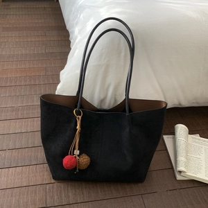Détail du sac cabas en daim noir avec breloques en peluche sur un sol en bois chic
