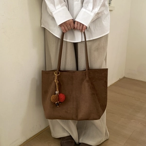 Détail du sac cabas en daim marron avec pendentif décoratif et coutures minimalistes