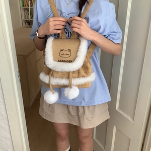 Detail of khaki canvas backpack featuring white plush trim, pom-pom drawstrings and cat print