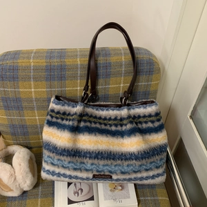 Large striped faux fur tote bag with brown leather straps on a cozy plaid sofa