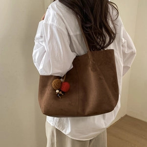 Détail d'un grand cabas en daim marron foncé avec pompons décoratifs sur l'épaule