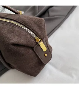 Detailed macro view of smooth gold zipper and brown suede material on the shoulder bag