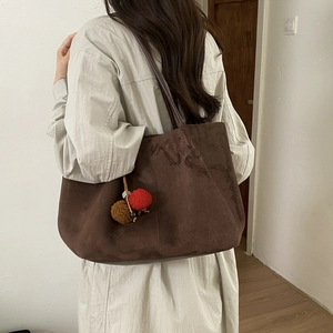 Détail du cabas en daim marron foncé avec un charmant pompon décoratif rouge et marron