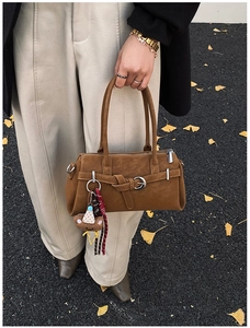 Close-up of brown suede Boston bag with leather strap detailing and cute bear charm decoration