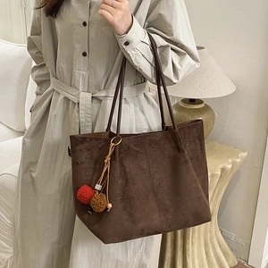 Grand sac cabas en daim marron avec pompons colorés porté par un mannequin chic