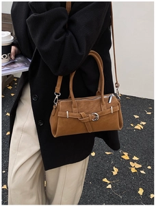 Close-up of brown matte leather crossbody bag with silver buckles in autumn street setting
