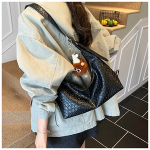 Detail of black woven leather tote bag with a decorative brown plush monster charm