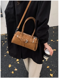 Close-up of brown suede crossbody bag with vintage buckle in an autumn street scene
