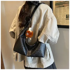 Close-up of black woven leather hobo bag worn by model with a brown plush charm