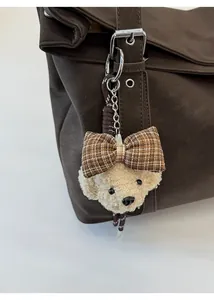 Gros plan d'un charme d'ours en peluche beige avec un nœud à carreaux sur un sac en cuir