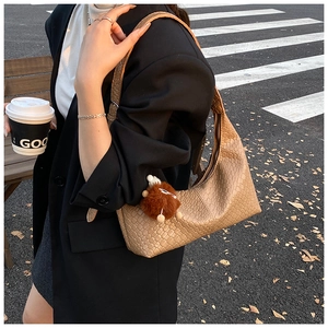 Detailed close-up of brown woven leather texture on a shoulder bag with plush ball charm