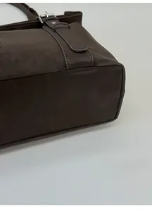 Gros plan sur le fond élargi et le cuir grainé de ce sac à bandoulière marron foncé