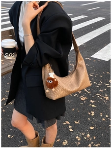 Detail of light brown woven shoulder bag featuring a soft faux leather texture and charm