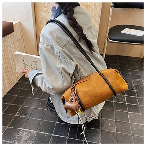 Detail of yellow-brown suede bowling shoulder bag with slim black strap and charms