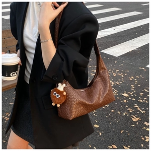 Detail of brown woven tote bag with plush monster charm worn on black blazer