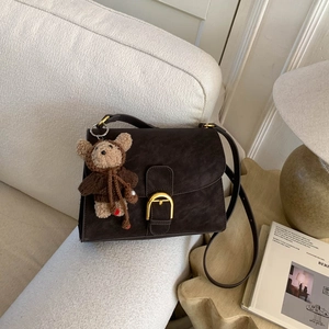 Detalle del bolso de ante marrón con hebilla dorada y colgante de oso de peluche