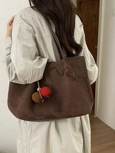 Grand sac cabas marron en daim avec pompons pelucheux porté à l'épaule, style minimaliste