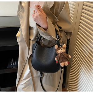 Detail of black pebbled leather crossbody bag featuring a cute plush bear charm accessory