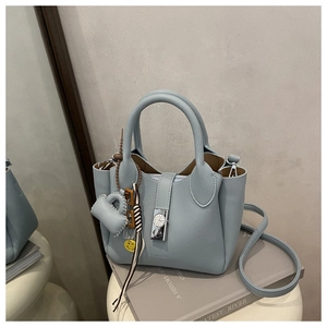 Bolso de cuero azul claro con un cierre metálico tipo reloj y varios colgantes de moda