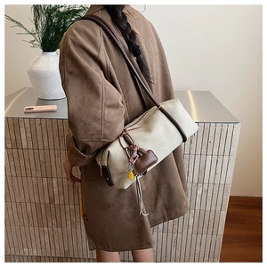 Detail of canvas shoulder bag with brown leather trim and heart charm on a model