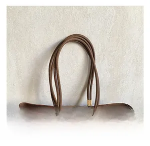Detail of a brown leather tote bag showing round handles and golden square metal buckles