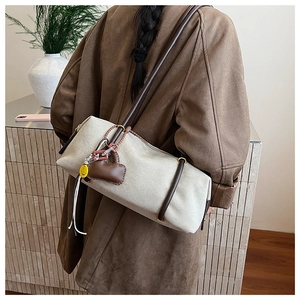 Detail of canvas cylinder bag with brown leather straps and heart-shaped pendant accessory