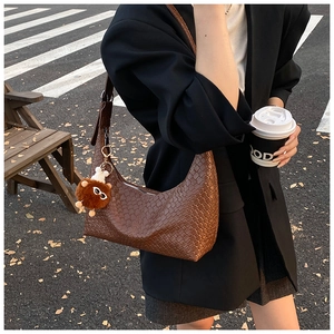 Detailed texture of brown woven hobo bag with cute plush bear charm on a city street