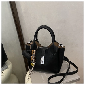 Detalle de bolso en piel negra con grano lichi, cierre de reloj plateado y accesorios